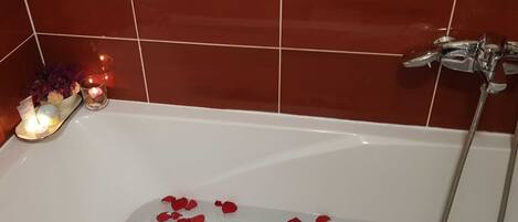 Una vasca da bagno con petali di rosa e candele, che evoca un'atmosfera romantica.