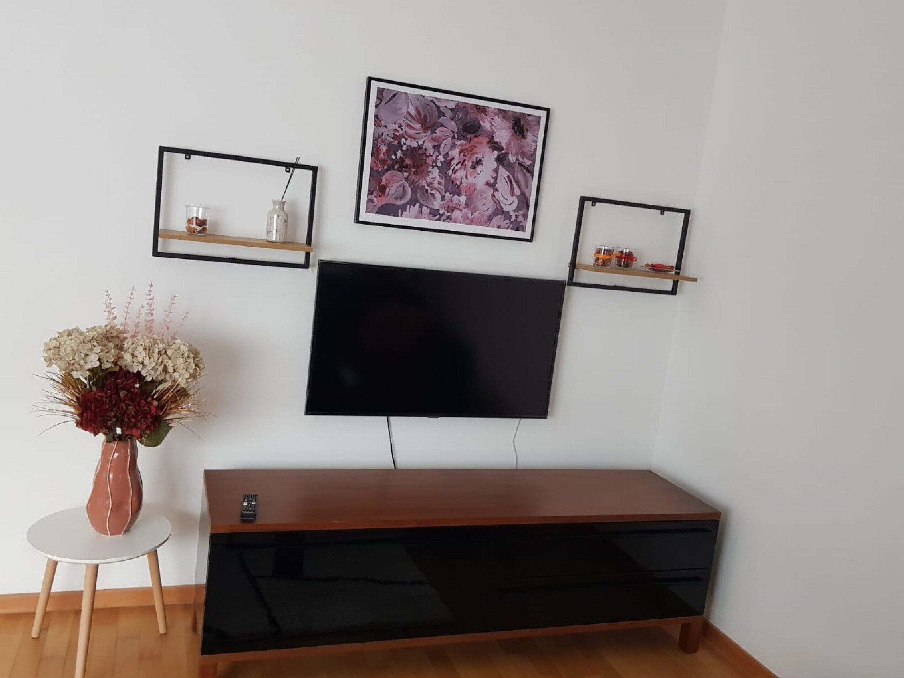 Una sala de estar moderna con un televisor de pantalla plana montado en la pared, un mueble de madera debajo y tres obras de arte enmarcadas en estantes superiores.