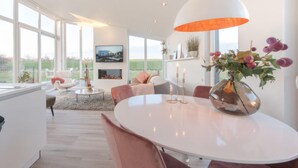 A modern interior with a round dining table, pink chairs, and a large window offering a view of the outdoors. - Dyke-view Stay With Terrace (Wemeldinge)