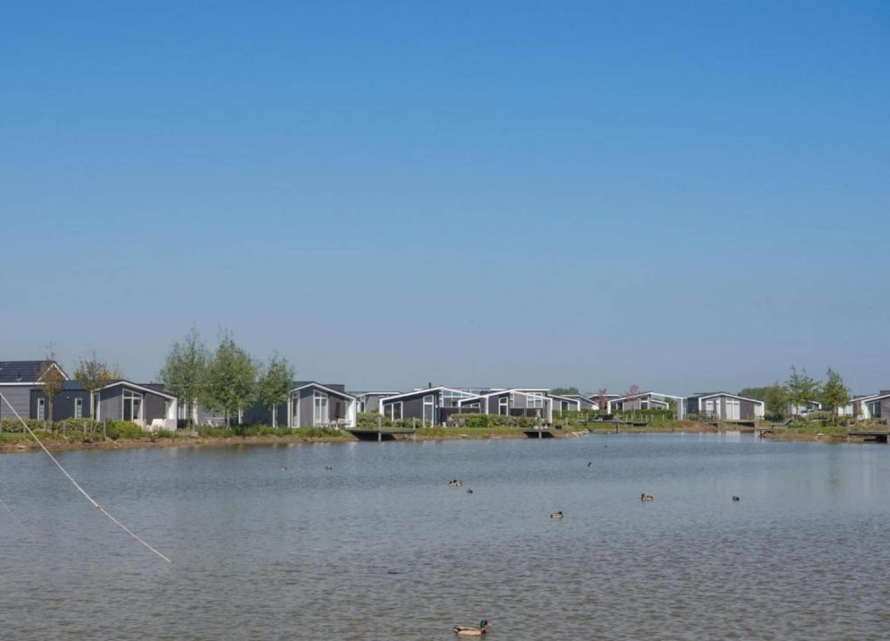 A row of modern, single-story houses by a calm lake with a clear sky.