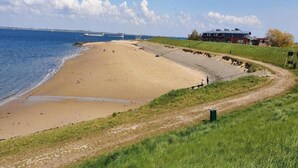 A beach with a clear view of the sea, a grassy area, and a building with a red roof. - Dyke-view Stay With Terrace (Wemeldinge)