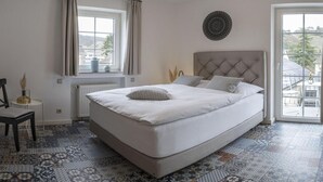 Quarto com uma cama grande, janela com cortinas, radiador e piso estampado.