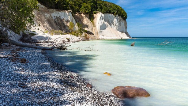 Una playa costera con acantilados blancos, agua turquesa cristalina y orilla de guijarros.