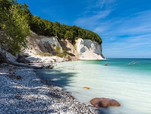 Una playa costera con acantilados blancos, agua turquesa cristalina y orilla de guijarros.
