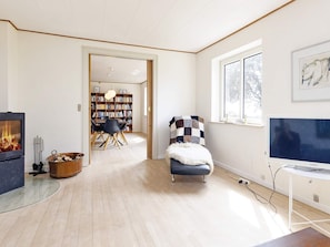 A modern living room with a fireplace, a television, a bookshelf, and a cozy chair. - Seaside Charm in Gedser - By Traum Ferienwohnungen (Gedser)