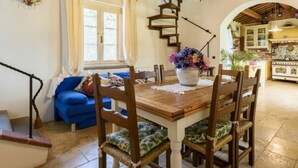 A dining area with a wooden table, chairs, and a chandelier. There is a staircase leading to another level, and a kitchen area is visible in the background. - Villa al Molino Comfortable Holiday Residence (Fauglia)