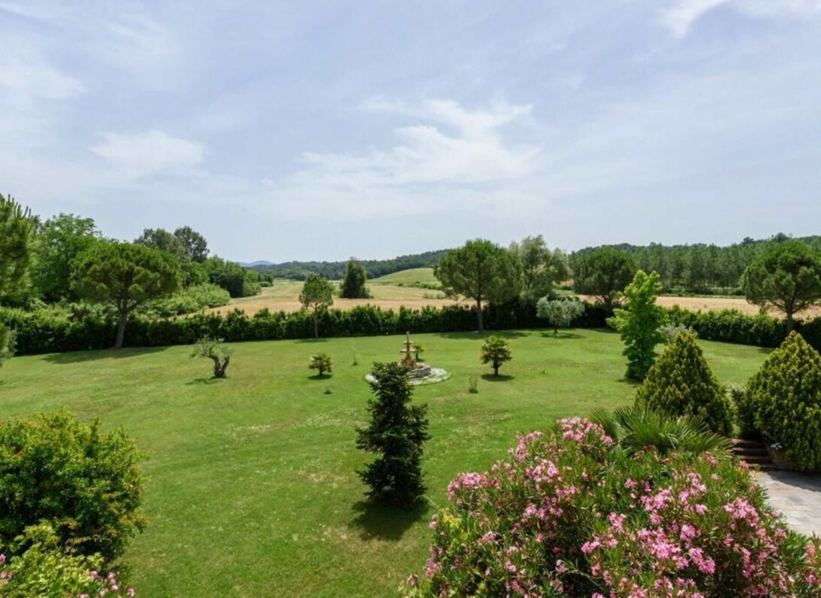 A well-maintained garden with a variety of trees and shrubs, a lawn, and a clear sky.