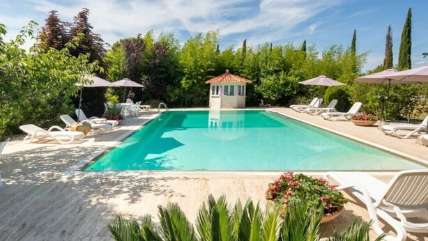 A rectangular swimming pool with a small gazebo in the center, surrounded by lounge chairs and umbrellas. - Villa al Molino Comfortable Holiday Residence (Fauglia)