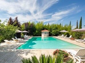 Ein rechteckiger Pool mit einer kleinen Laube in der Mitte, umgeben von Liegestühlen und Sonnenschirmen.