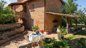 A rustic brick house with a patio area featuring a table set for dining, surrounded by potted plants and a pergola. - Villa al Molino Comfortable Holiday Residence (Fauglia)