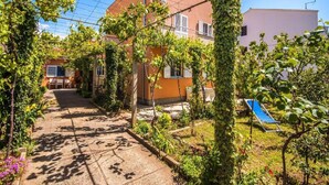 Un patio con una pérgola cubierta de hiedra, un toldo azul y un edificio con un reloj.