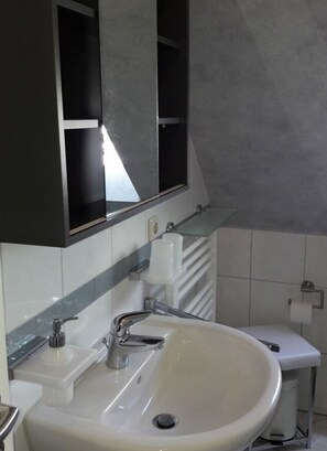 A bathroom with a white sink, a mirror, and a towel dispenser. - Holiday Home at Buttring (Krummhoern)