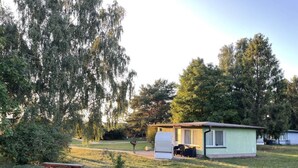 A small, single-story building with a flat roof, likely a mobile home or a small cabin, situated in a grassy area with trees in the background. - 08 am Haff Modern Retreat (Kamminke)
