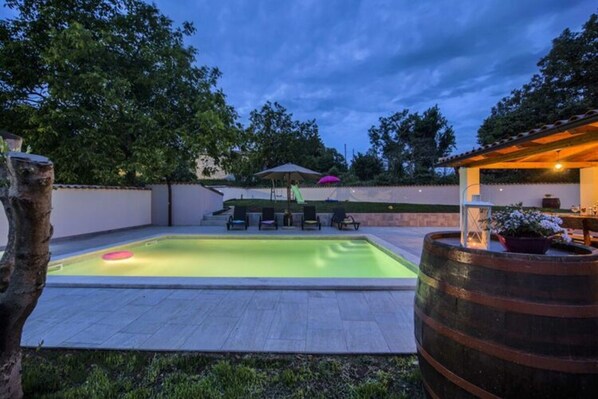 A rectangular swimming pool with a green hue, surrounded by a tiled deck. There are lounge chairs and a small bar area with a lantern. - Villa G With Pool in Barban (Barban)