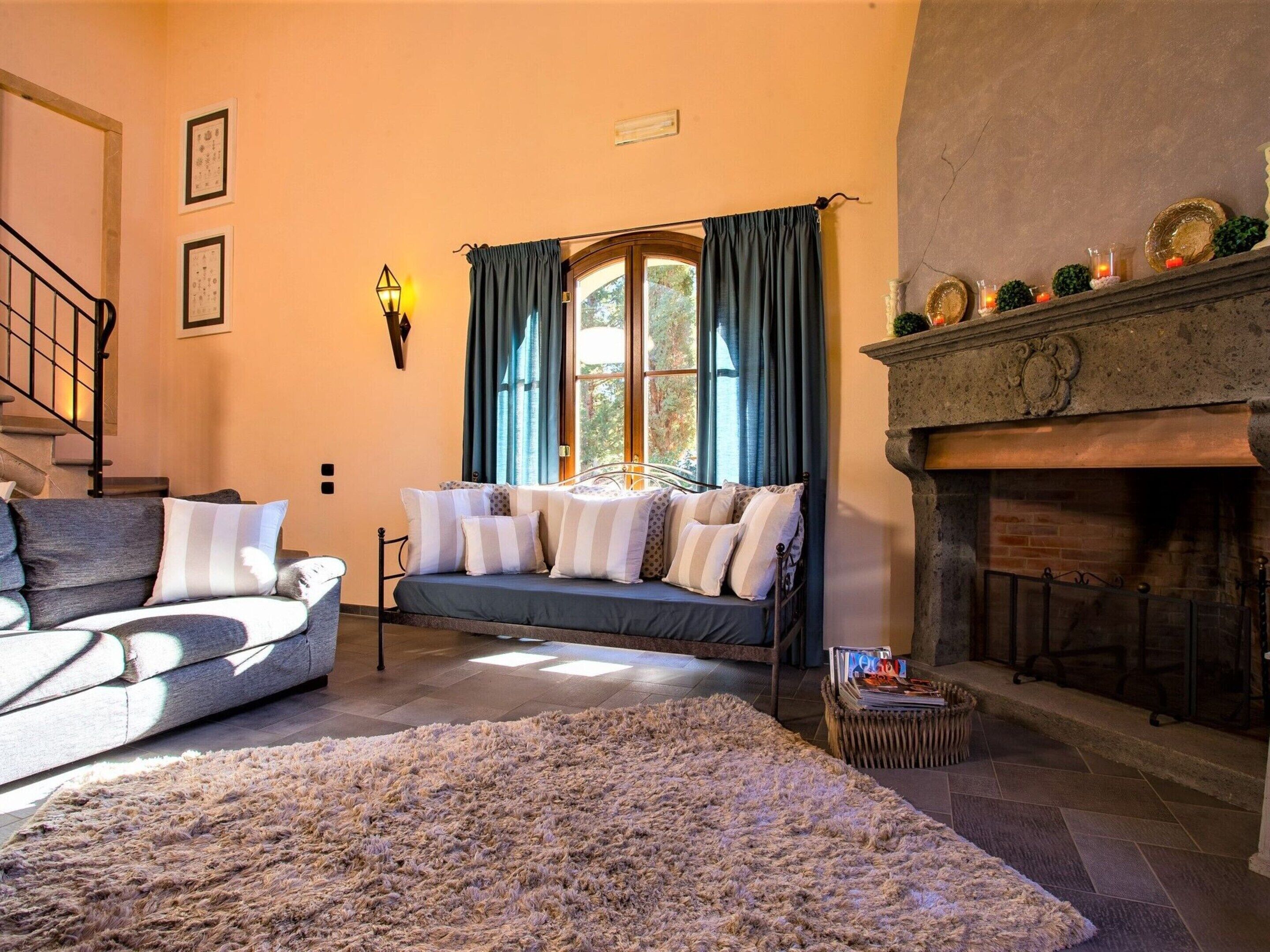 A cozy living room with a sofa, a rug, a fireplace, and a window with curtains.