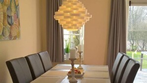 A dining area with a rectangular table, dark upholstered chairs, and a unique hanging light fixture. - Villa "De Banjaard Zeeland" (Kamperland)
