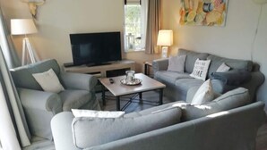 A living room with a grey sofa set, a flat-screen TV, a coffee table, and two lamps. - Villa "De Banjaard Zeeland" (Kamperland)