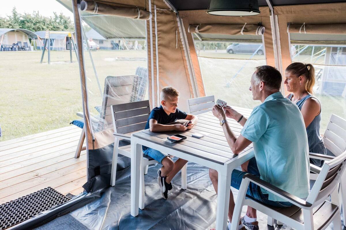 Un espace extérieur abrité, avec une table et des chaises, où une personne est assise en train de jouer aux cartes, et d’où l’on peut admirer le paysage.
