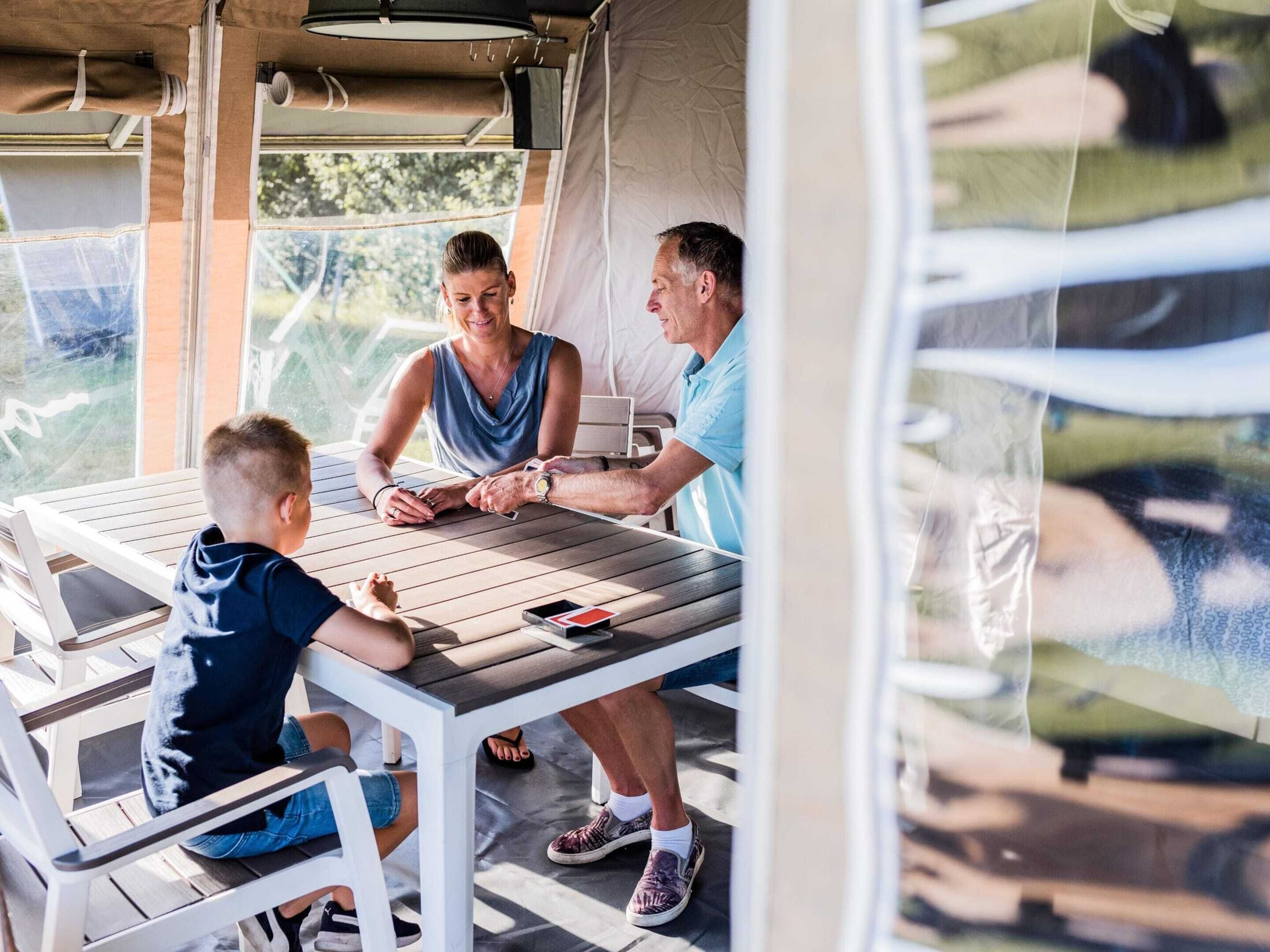 Un espace extérieur abrité avec une table et des chaises, une personne tenant un téléphone intelligent et une autre personne se tenant à proximité.