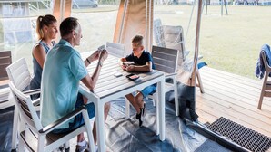 A family of three at a table with a view of a grassy area and tents in the background.