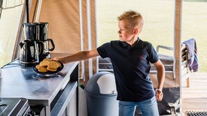 A person serving cookies from a tray at a table with a coffee maker.