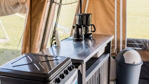 A kitchen area with a portable gas stove, a coffee maker, and a trash bin.