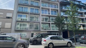 Un immeuble résidentiel à plusieurs étages, doté de balcons, avec des voitures garées et un ciel dégagé.