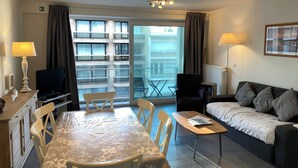 Une chambre d’hôtel moderne dotée d’un coin repas, d’un canapé, d’une télévision et d’un balcon offrant une vue sur l’immeuble.
