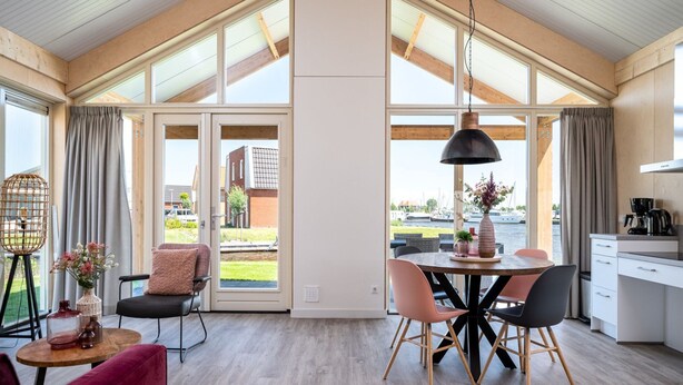 A spacious room with a high ceiling, large windows, a dining area with a table and chairs, and a kitchenette. - House for the Disabled, Holiday Park in Friesland (Akkrum)