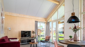 A modern living room with a TV, red sofa, and a dining area with a table and chairs. - House for the Disabled, Holiday Park in Friesland (Akkrum)