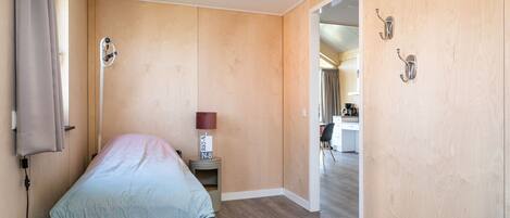 A bedroom with a bed, bedside table, lamp, and a view into a kitchen area.