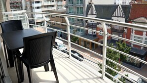 En balkon med et bord og stole, der ud til en gade med bygninger og biler.