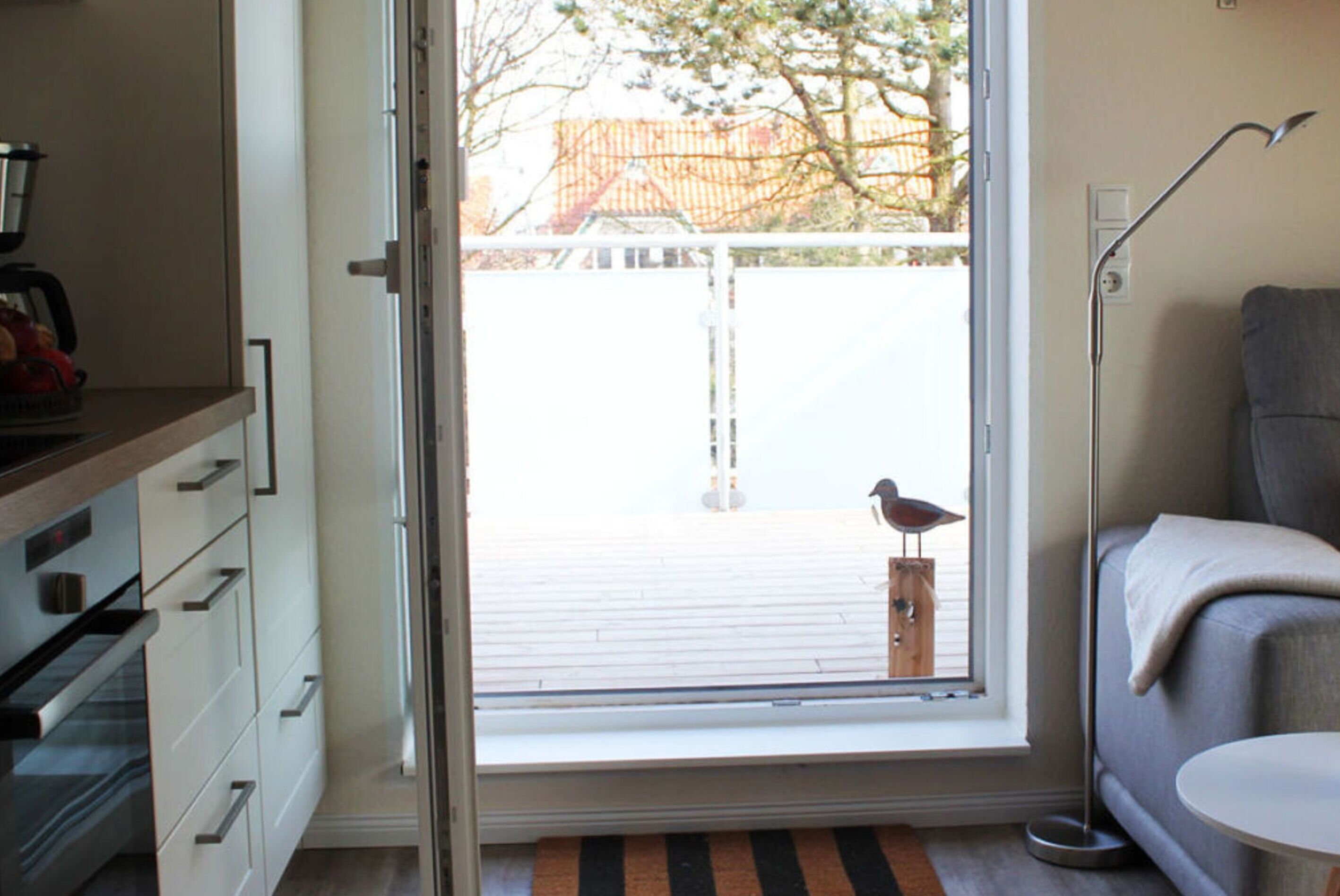 A room with a sliding glass door leading to a deck, a sofa, a coffee machine, and a small table.