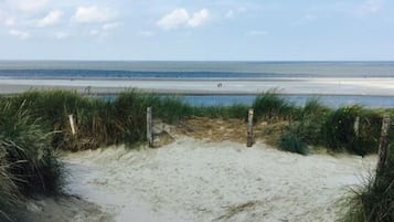 A wooden boardwalk leading to a beach with sand and grass on either side.