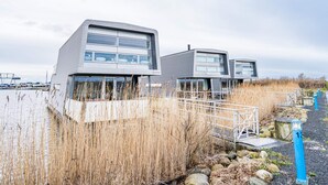 Moderni rakennus, jossa on tasakatto ja suuret ikkunat. Se sijaitsee lähellä vesistöä, ja taustalla näkyy laituri.