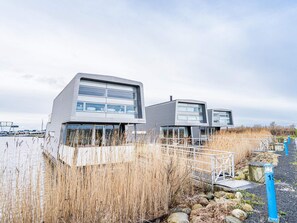 A modern building with a flat roof and large windows, situated near a body of water with a dock in the background. - 5 Star Holiday Home in Hemmet (Hemmet)