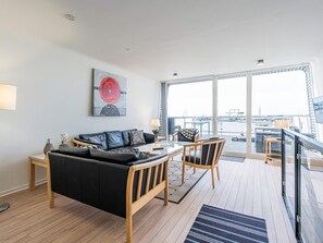 A modern living room with a sofa, a coffee table, and a view of the marina through large windows. - 5 Star Holiday Home in Hemmet (Hemmet)