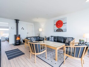 A modern living room with a central fireplace, a dining table, and a sofa set. - 5 Star Holiday Home in Hemmet (Hemmet)