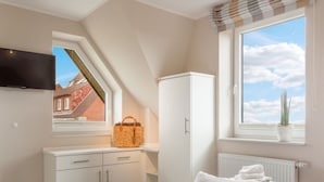 Ein Schlafzimmer mit einem Bett, einem weißen Kleiderschrank, einem Fenster mit Blick zum Himmel und einem Korb auf der Fensterbank.