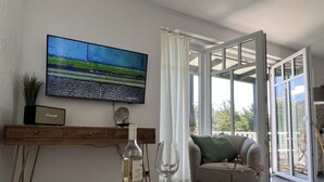 A modern living room with a wooden table, a television mounted on the wall, and a sofa with a view to the outside. - Beach House "blanker Hans" (Sylt)