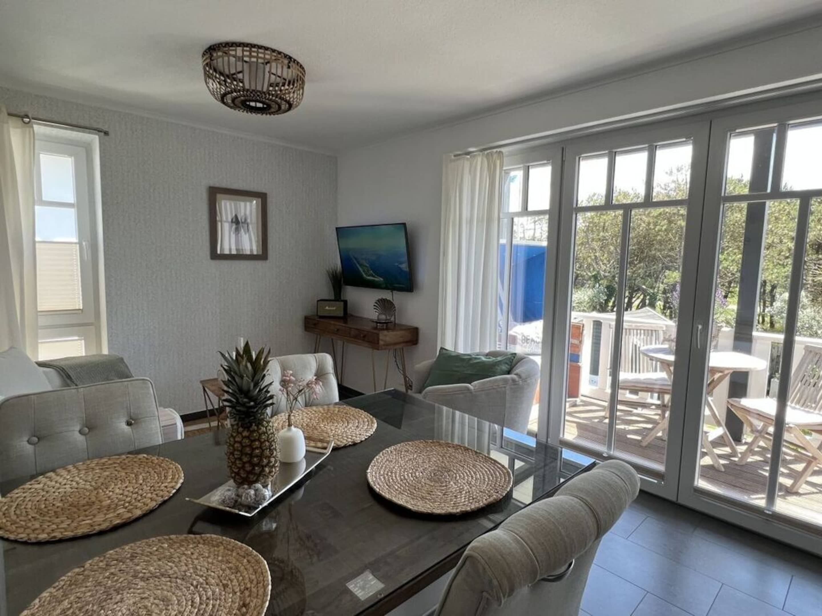A modern living room with a glass dining table, cushioned sofas, and a large window with a view of the outdoors.