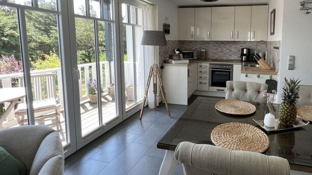 A modern kitchen with large windows, a dining area with a glass table, and a view of the outdoors. - Beach House "blanker Hans" (Sylt)