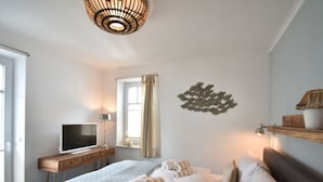 A bedroom with a bed, a desk with a TV, a window with curtains, and a wall decoration. - Beach House "blanker Hans" (Sylt)