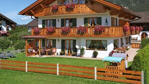 A two-story wooden house with balconies, a front porch, and a well-maintained lawn. - Holiday Apartment "wetterstein" (Kruen)