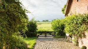Een geplaveid pad dat leidt naar een landelijk, bakstenen gebouw met een houten poort.