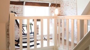 Een loftachtige kamer met een schuin dak, zichtbare houten balken en een witte balustrade.