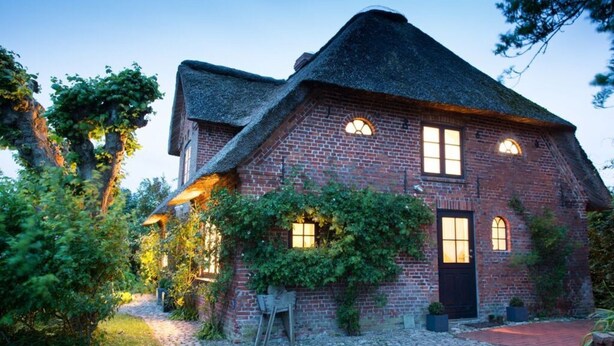 Een traditioneel bakstenen huis met een steile kap, een voordeur en een kleine tuin met een straatje van keien.