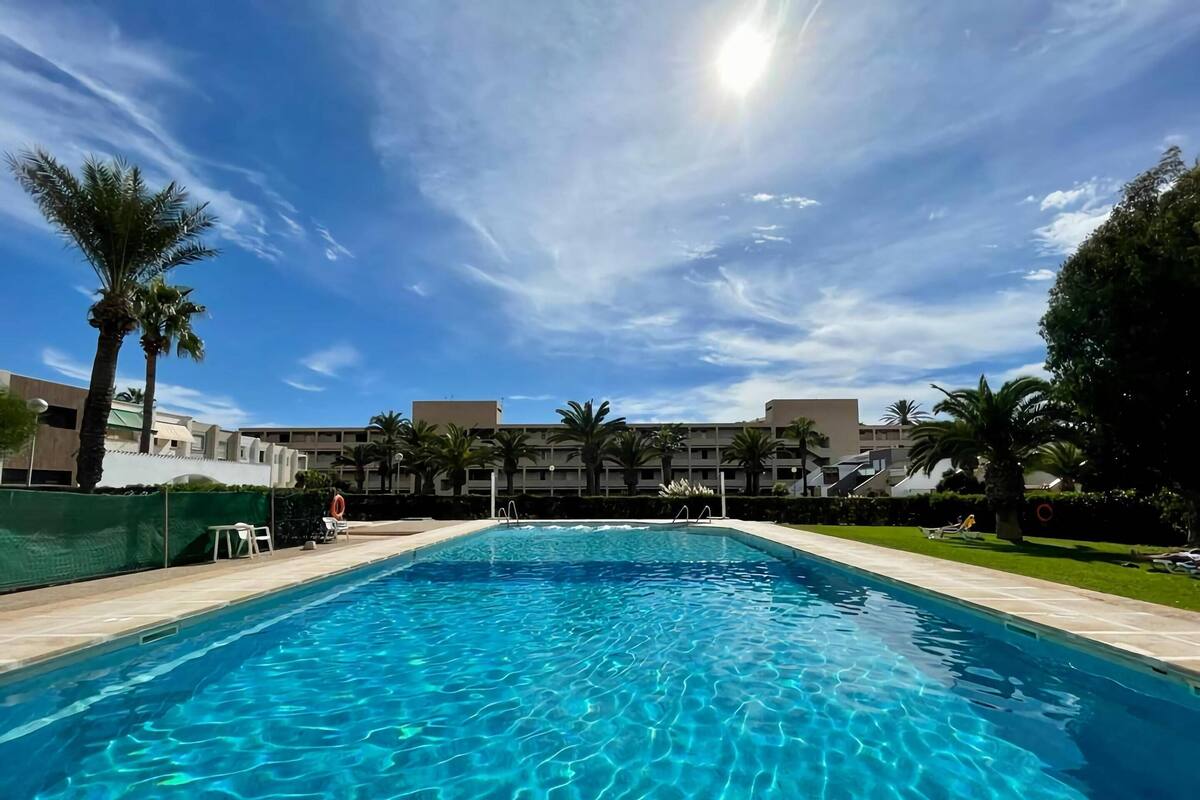 Ein Pool mit klarem Wasser, umgeben von Palmen und einem Gebäude im Hintergrund.