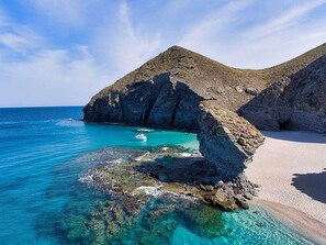 A coastal landscape with clear turquoise waters, rocky formations, and a sandy beach. - Belvilla by OYO Apartment in Vera Playa (Vera)