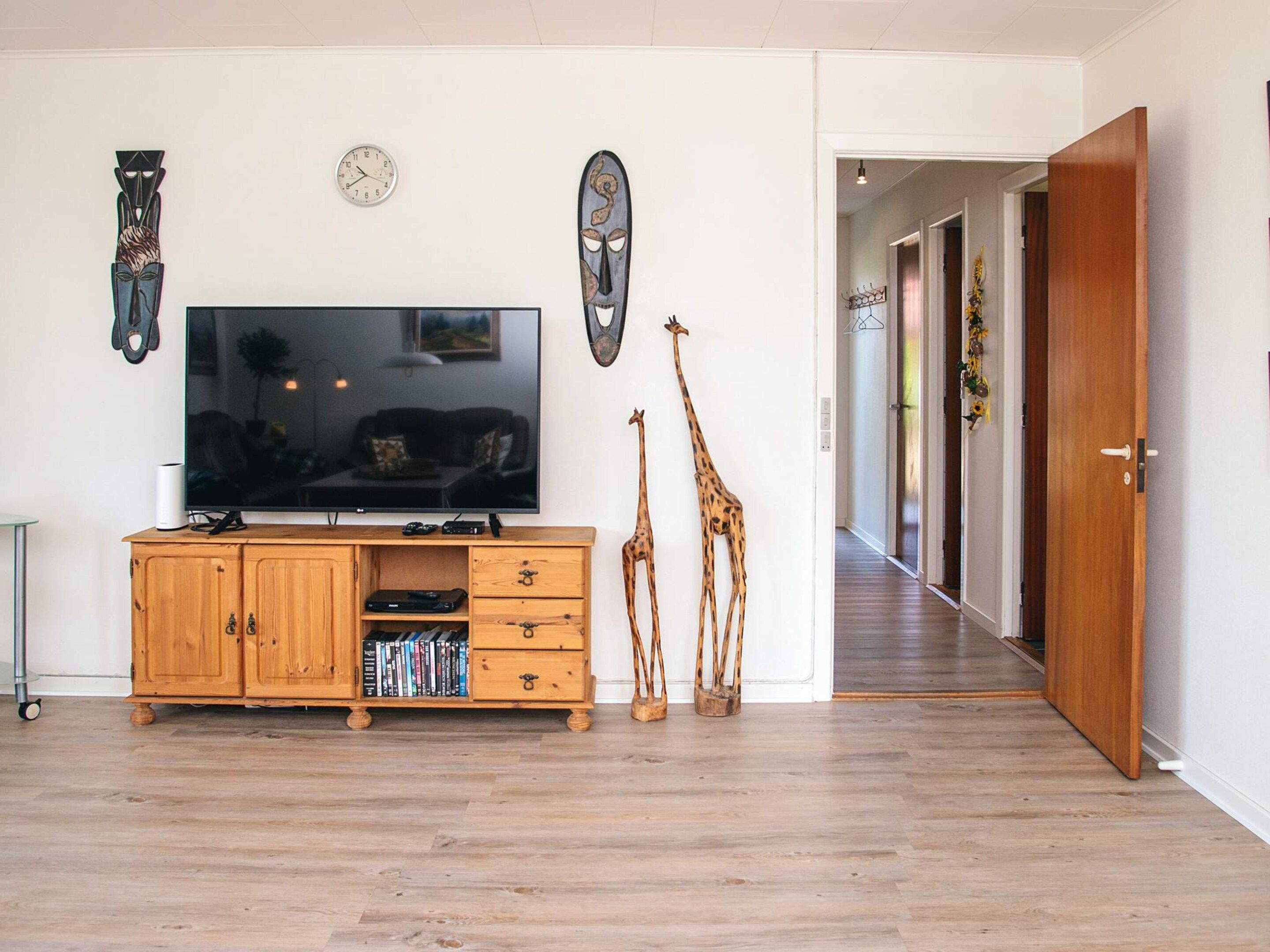 Una sala de estar con un televisor de pantalla plana, un mueble de madera para equipo multimedia, dos esculturas de jirafa y un reloj en la pared.